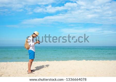 Summer Day.  Happy smiling caucasian tourist asian young man holding camera for take a photo check in on the beach. Summer and Travel Concept.