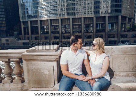 young and stylish lovers couple in white t-shirts and blue jeans walking in a big city near tall buildings