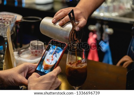 Man taking a photo of barista pour red ruby shake coffee with smartphone