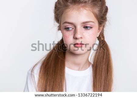 Bright freckles. Tranquil light-haired girl with two long tails wearing plain white t-shirt and looking down
