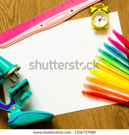 microscope, multi-colored pens, ruler and alarm clock on a white sheet of paper on a wooden background, copy space