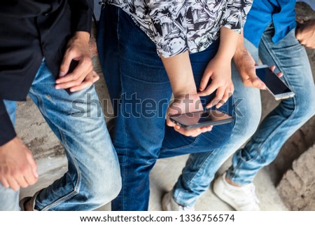 Close up of only hands and legs of teenager sitting on a wall and using smart phones and spending time with friends.