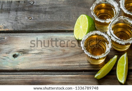 Tequila in a shot glass with lime slices. On wooden background