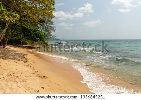 Sandy beach with waves coming in and rain forest dawn to the water and a cloudy sky in background, picture from Rach Tram beach on Phu Quoc Island, Vietnam.
