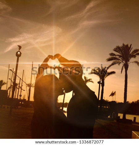 Silhouette of happy young couple love outside , showing hearts on hands. Twilight
