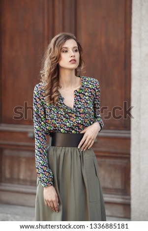 Stylish brunette girl dressed in motley blues and long gray skirt poses in the city street on a sunny day