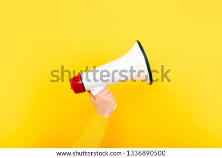 megaphone in hand on a yellow background, attention concept announcement Royalty-Free Stock Photo #1336890500