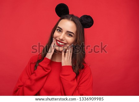 Happy brunette girl wearing bright red sweatshirt and red lipstick posing in cute mouse ears on red background 