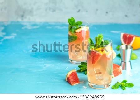 Grapefruit and mint gin tonic cocktail, refreshing drink with ice. Cold summer citrus refreshing drink cocktail or beverage with ice on blue concrete surface.