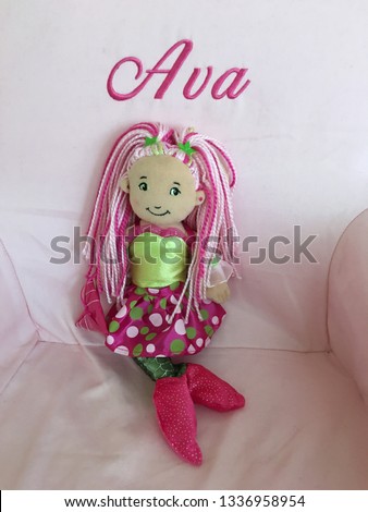 The little mermaid sitter in the chair.  The chair is light pink.  The mermaid has green shirt and polka dot skirt.