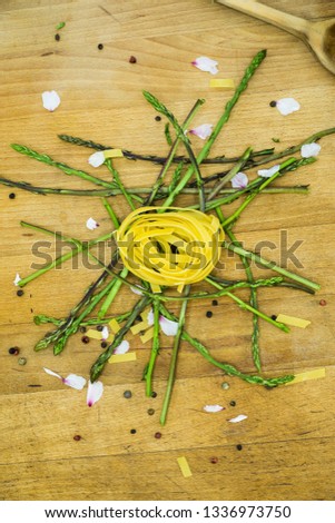 Fresh pasta on a pile of fresh asparagus fallen on a rustic wood, with pepper and flowers. Preparations for a healthy dinner, for people who love cooking. Vertical image.