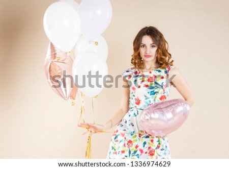 Girl with helium balloons in different clothes, on a beige background. Pastel colors photo. Emotions and poses. Close up.