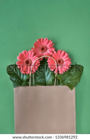 Coral gerbera daisy flowers and craft papper shopping bags on green paper background, Springtime sale concept image with copy-space