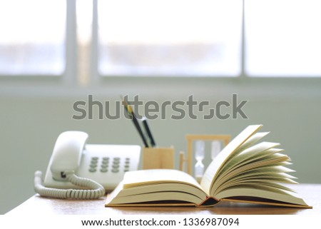 Backlit picture, open book on the desk office phone as background selective focus and shallow depth of field