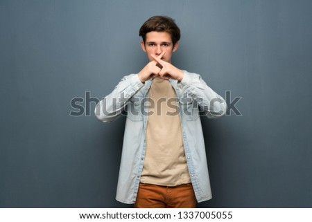 Teenager man with jean jacket over grey wall showing a sign of silence gesture