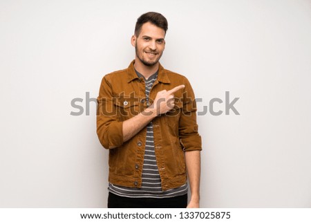 Handsome man over white wall pointing to the side to present a product