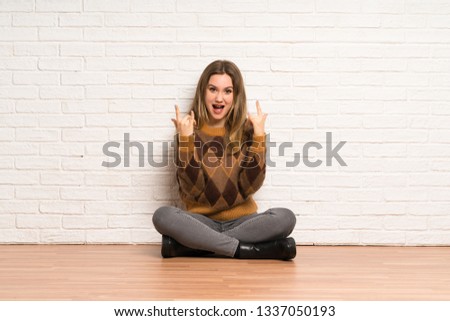 Teenager girl sitting on the floor making rock gesture