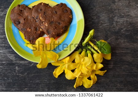 Heart-shaped chocolate cookies in a plate with yellow flowers on a wooden background