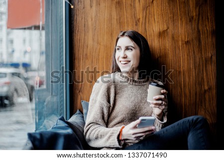 Charming woman with beautiful smile reading good news on mobile phone during rest in coffee shop, happy beautiful model watching her photo on cell telephone while relaxing in cafe during free time