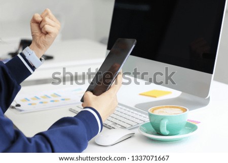 Hands are using smart phones. There is a computer screen on the desk.