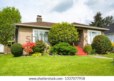 Modest residential house with concrete pathway over green lawn of the front yard on cloudy day Royalty-Free Stock Photo #1337077958
