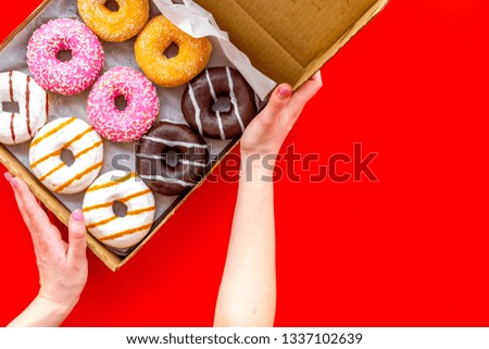 Glazed decorated donuts in box and hands on red background flat lay mock up