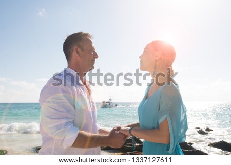 Couple holding each others hands and looking each other. Turquoise water is behind them. Backlight picture. Lens flare at the image