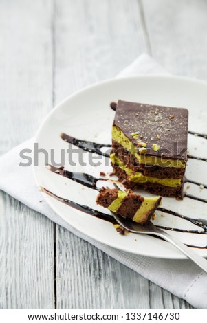 one piece of chocolate three-layer cake on a white plate on grey wooden table