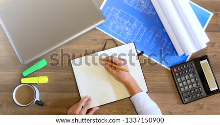 Female hand in a shirt writes in a leather notebook. Computer, cup of coffee, graphics, drawings, calculator on the table in the office. Business and Finance.