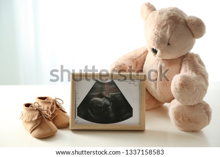 Ultrasound picture, teddy bear and baby shoes on table against light background. Space for text