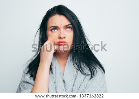 A young beautiful girl in a gray robe troraet his cheek, thinking about fat cheeks, about excess weight, and that it is time to lose weight on a gray-white studio background Royalty-Free Stock Photo #1337162822