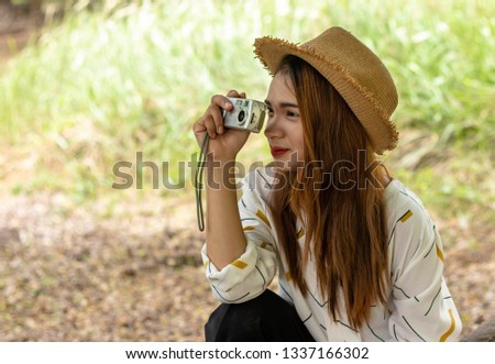 Women tourists women white skin lovely brown hair wearing a basketry hat wear white shirt wearing black pants in hand have a camera traipse photograph nature.