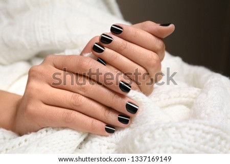 Woman with black manicure holding knitted fabric, closeup. Nail polish trends