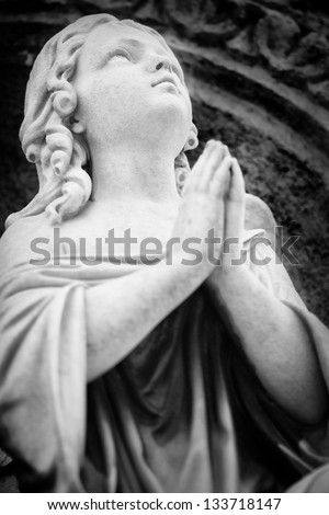 Black and white  image of an old angel sculpture praying and looking at the sky