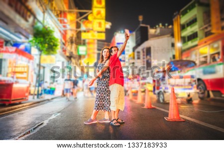 Asian couple tourist taking photo in Yaowarat walking street, Two people traveler selfie with smartphone in Chinatown, Landmark travel Bangkok Thailand China Town night light, Tourism destination Asia