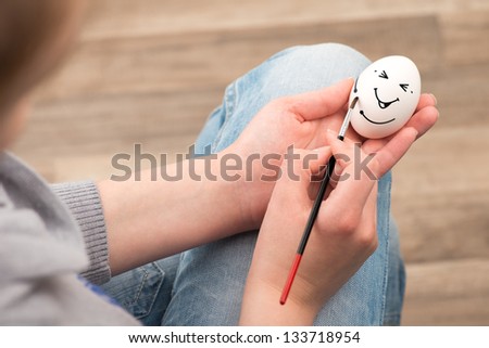 The girl draws with a brush on an white egg. Egg laughs.