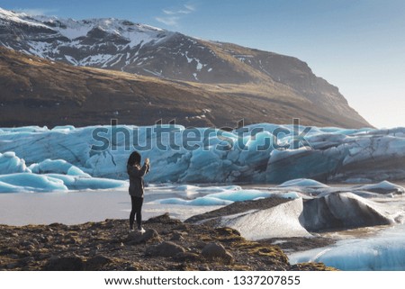 Back view of female tourists photographer taking picture of beautiful evening scenery of Skaftafell glacier Vatnajokull national park in Iceland is blue and cold is iceberg and best place for turism.