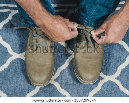 A man in a blue jeans tying up shoelaces on brown leather shoes