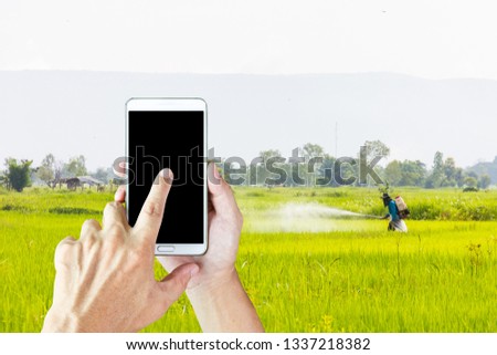 Man use mobile phone, blur image of farmer spray insecticides in the field.
