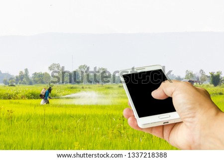 Man use mobile phone, blur image of farmer spray insecticides in the field.