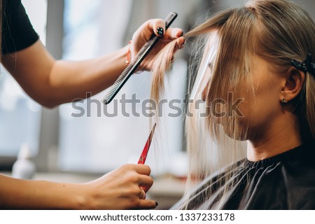 Hairdresser cuts hair by scissors beautiful blonde girl Royalty-Free Stock Photo #1337233178