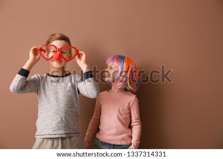 Little children in funny disguise on color background. April fools' day celebration