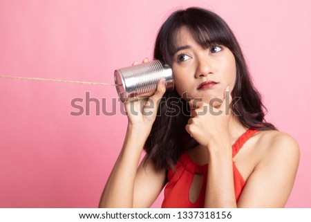 Young Asian woman hearing with tin can phone and thinking on pink background