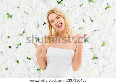 excited young woman showing thumbs up and funny grimacing on white floral background