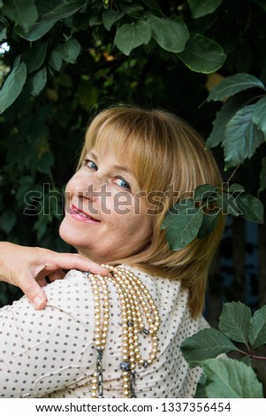 Portrait of happy beautiful blonde woman with pearls in summer park