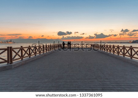 Wooden dock with people against blue cloudy sky after rain at sunset.