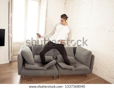Portrait of young happy teenager male listening to music in headphones singing and dancing on couch sofa having fun at home. In positive emotions and happiness,Leisure Music and technology concept.