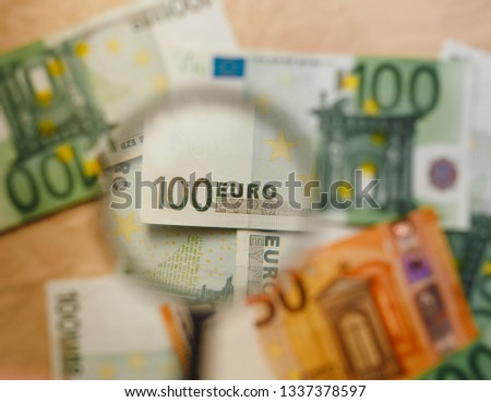 Checking a 100 euro banknote with a magnifying glass