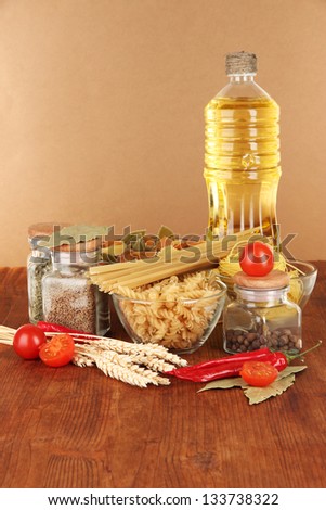 Different types of pasta, spices, tomatoes on a wooden table on brown background