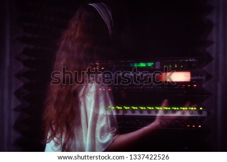 A girl in a white dress with long hair sings behind a microphone. Professional singer performs vocals in the recording Studio. Reflection in the glass of a woman who sings